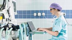 Healthcare worker using laptop next to medical equipment
