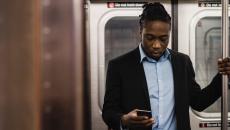 A person in a suit jacket looks down at his cellphone while standing and riding the subway.
