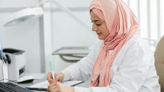 A hijab-wearing nurse filling out a patient form on a desk